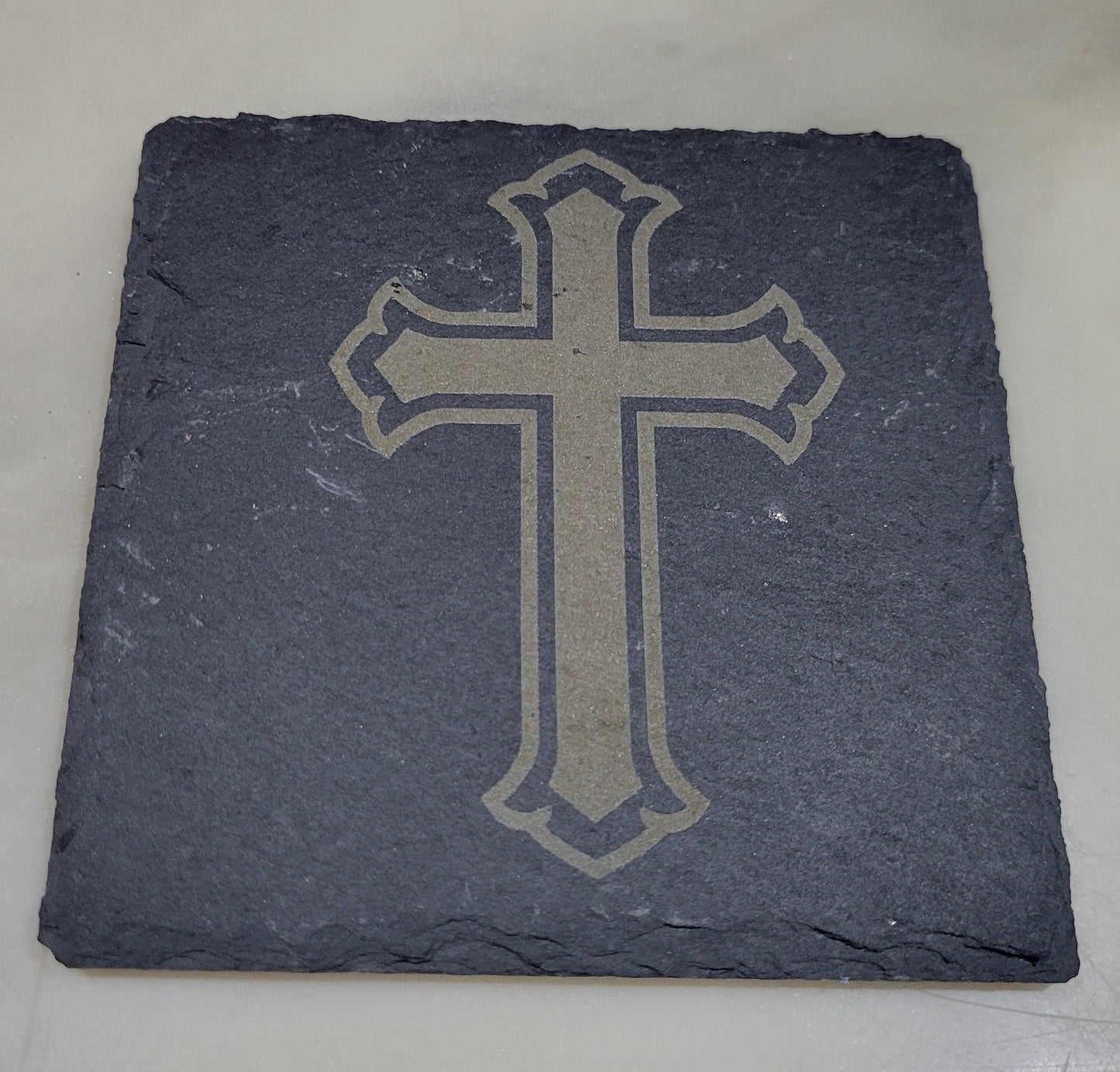 Slate coaster with a cross design on a light marble background
