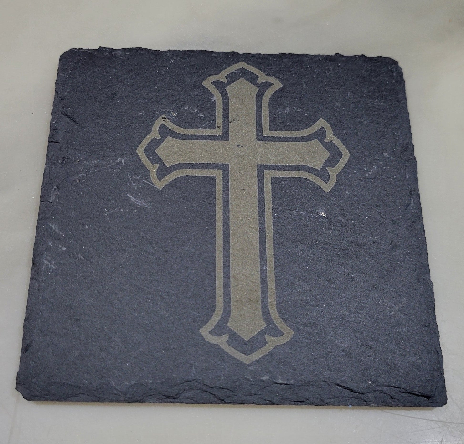 Slate coaster with a cross design on a light marble background