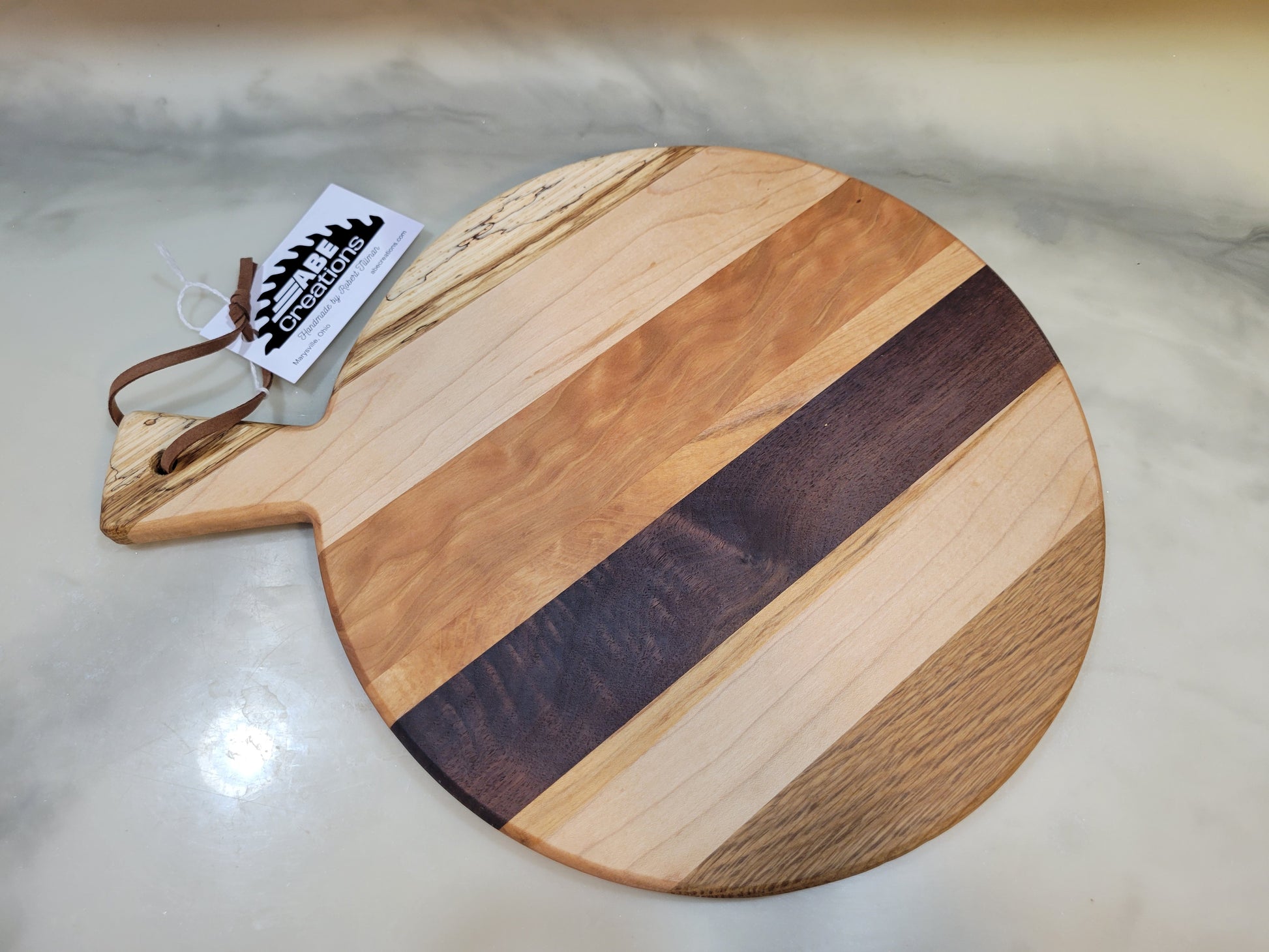 Round wooden cutting board with a handle on a light marble surface.