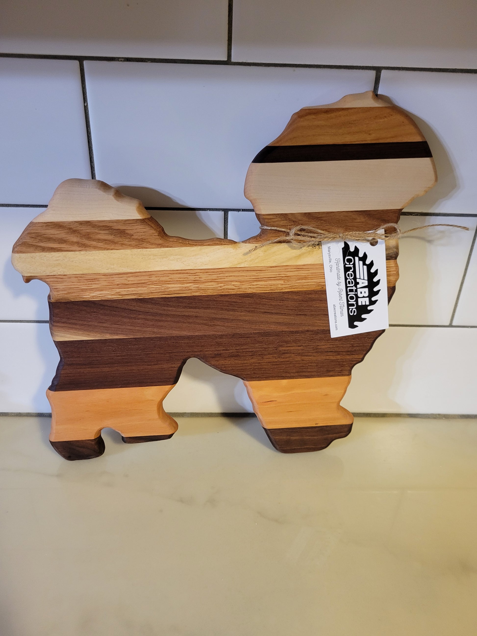 Wooden cutting board with a unique shape on a tiled floor, branded 'ABE Creations'.