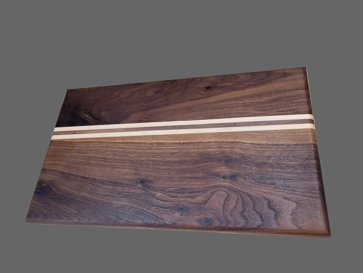 A rectangular wooden cutting board with a dark walnut wood grain finish and two thin light-colored inlay stripes across the center, resting on a light marble surface.