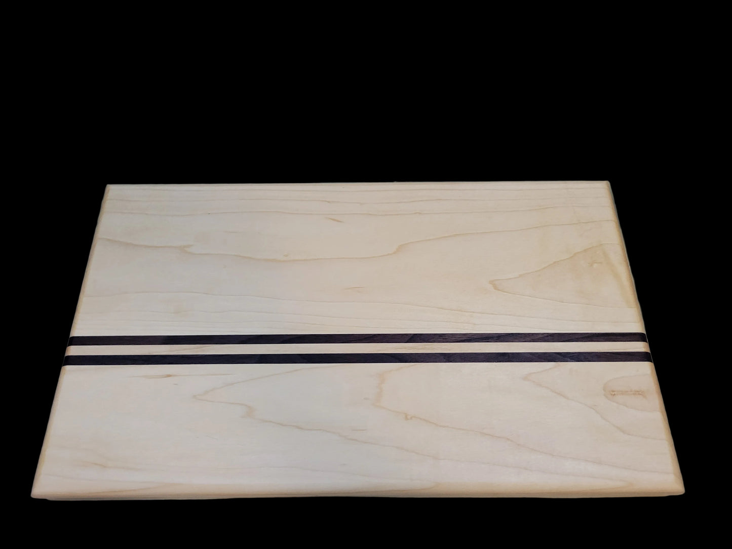A rectangular light wood cutting board with two parallel dark inlay stripes across the center, photographed on a light marble-like surface.