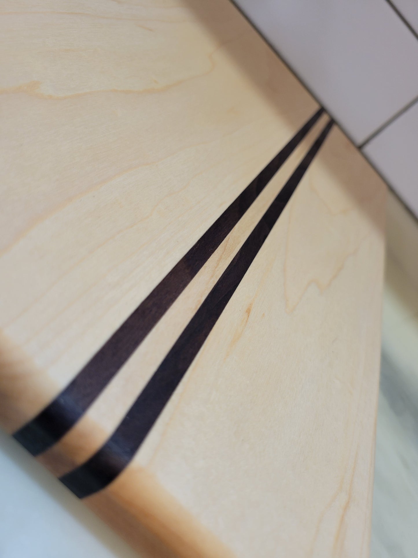 Close-up of a light natural wood cutting board with two dark brown inlaid stripes running diagonally across the surface.