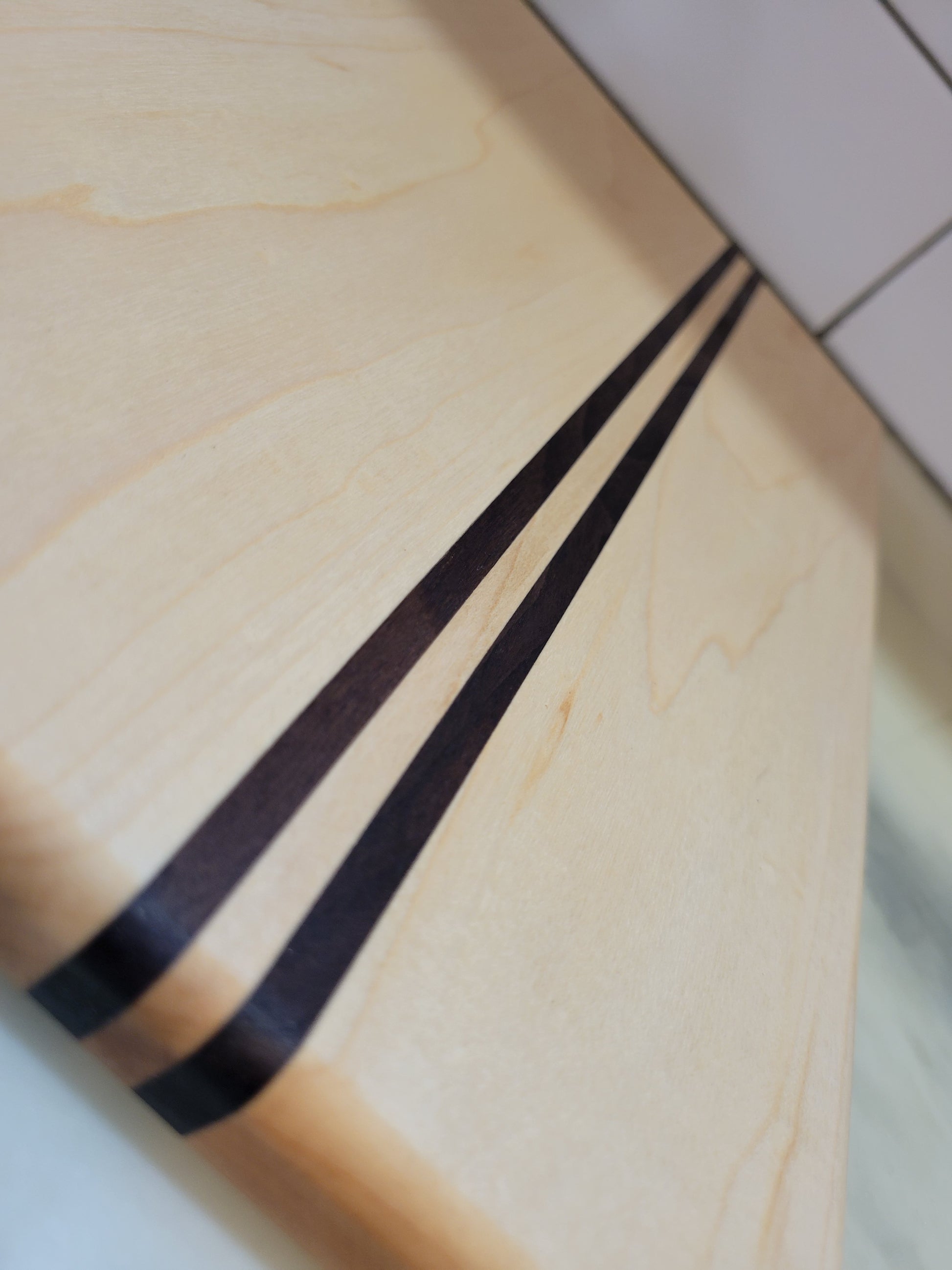 Close-up of a light natural wood cutting board with two dark brown inlaid stripes running diagonally across the surface.